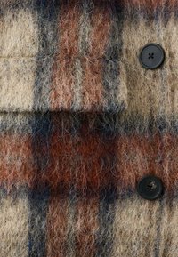 Tela de mezcla de lana con un patrón de cuadros multicolor que presenta tonos de naranja, marrón, beige y negro. Incluye un detalle de botón negro.