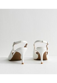Scarpe slingback bianche con tacco alto, in pelle liscia, con tacco sottile e cinturino alla caviglia regolabile, dotate di una soletta colorata in tono cuoio.