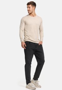 Chemise beige à manches longues au design ajusté, associée à un jean noir et des baskets crème. L'ensemble présente une texture simple et lisse.