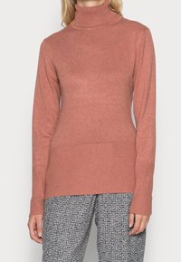 Maglione a collo alto rosa chiaro con maniche lunghe, texture a coste e silhouette aderente, abbinato a pantaloni a fantasia bianco e nero.