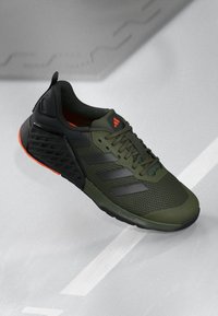 Chaussure de sport verte avec tige en mesh, accents noirs, trois bandes sombres, intérieur orange et semelle texturée pour l'adhérence.