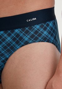 Blaue und schwarze Karoblende mit einem marineblauen Elastikbund, auf dem der Markenname "CALIDA" in weißen Buchstaben steht. Glatte Stoffstruktur.