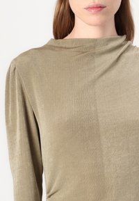 Olive green top made of soft, textured fabric. Features a high neckline and subtle pleats at the shoulders. Simple and fitted design.