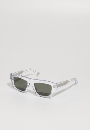 Occhiali da sole oversize trasparenti con lenti verde scuro, caratterizzati da una montatura spessa e dettagli metallici texturizzati sulle tempie.