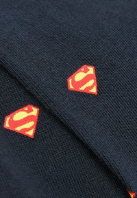 Tejido de punto azul marino con parches de logo de superhéroe en rojo y amarillo. Superficie texturizada; diseño de logo geométrico en colores contrastantes.