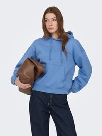 Lichtblauwe katoenen hoodie met een kangoeroezak, trekkoord en geribbelde manchetten, gecombineerd met donkerblauwe denim jeans en een bruine tas.