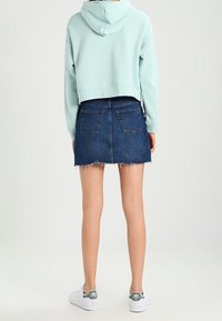 Mintunvihreä lyhyt huppari, sininen farkkuhame revityllä reunuksella ja valkoiset lenkkarit vihreillä yksityiskohdilla. Takakatsaus asuun.