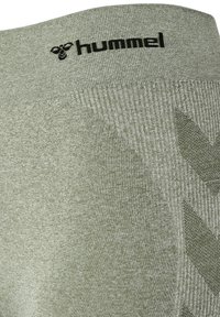 Zbliżenie jasnozielonej dzianiny prążkowanej z czarnym logo „hummel” i wzorem jodełki na pasie.