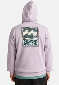 Felpa viola con un grande grafico sul retro che presenta onde e il testo "BILLABONG". Il materiale sembra morbido con una vestibilità comoda.