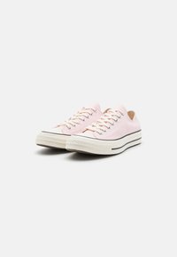 Sneakers in tela rosa chiaro con suole in gomma bianca, striscia orizzontale nera e fori per lacci. Punta rotonda e lacci piatti.
