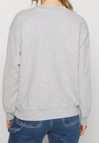 Sweat-shirt gris avec une finition texturée, col rond côtelé et coupe décontractée. Présente des épaules tombantes et un ourlet droit. Porté avec un jean bleu.