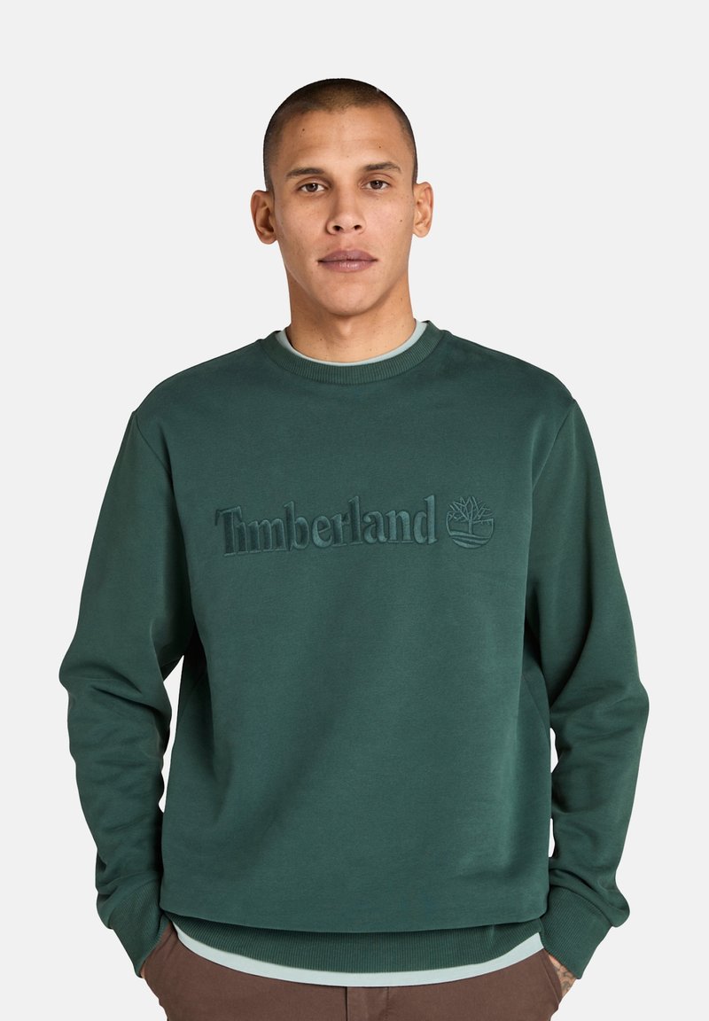Felpa in cotone verde scuro con colletto a costine, caratterizzata da un logo "Timberland" in rilievo e una grafica di un albero sul davanti.