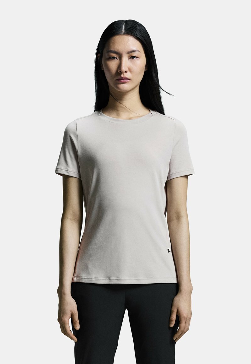 Camiseta ajustada color beige claro, hecha de una tela suave. Presenta mangas cortas, un escote redondo y un pequeño logo en la parte inferior izquierda.