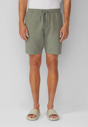 Light green, textured shorts with an elastic waistband and drawstring, worn with beige slide sandals. Simple, relaxed fit.