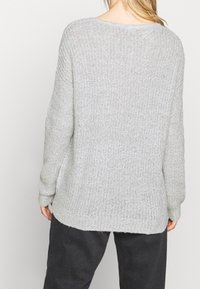 Pull en maille gris clair à coupe ample, tissu texturé et ourlet courbé. Il comporte des manches longues et un col décontracté.