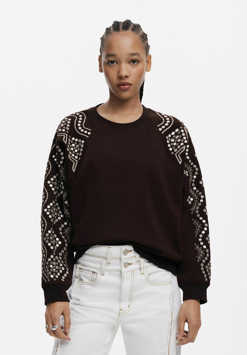 Sweatshirt maro cu cusături decorative din alb și embellishments pe mâneci, asociat cu blugi albi cu talie înaltă, având detalii cu nasturi.