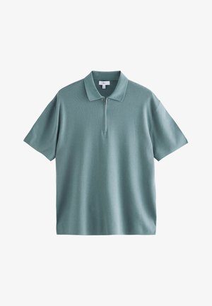Polo van zachte teal kleur met korte mouwen. Voorzien van een korte ritssluiting, zachte gebreide textuur en een klassiek kraagontwerp.