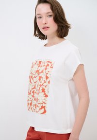 Weißes T-Shirt mit großem Blumenmuster in Koralle und Creme. Kurze Ärmel, runder Halsausschnitt und aus weichem Baumwollmaterial.