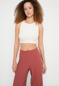 Top curto canelado creme combinado com calças terracota de cintura alta e pernas largas. O tecido é macio com uma textura subtil.