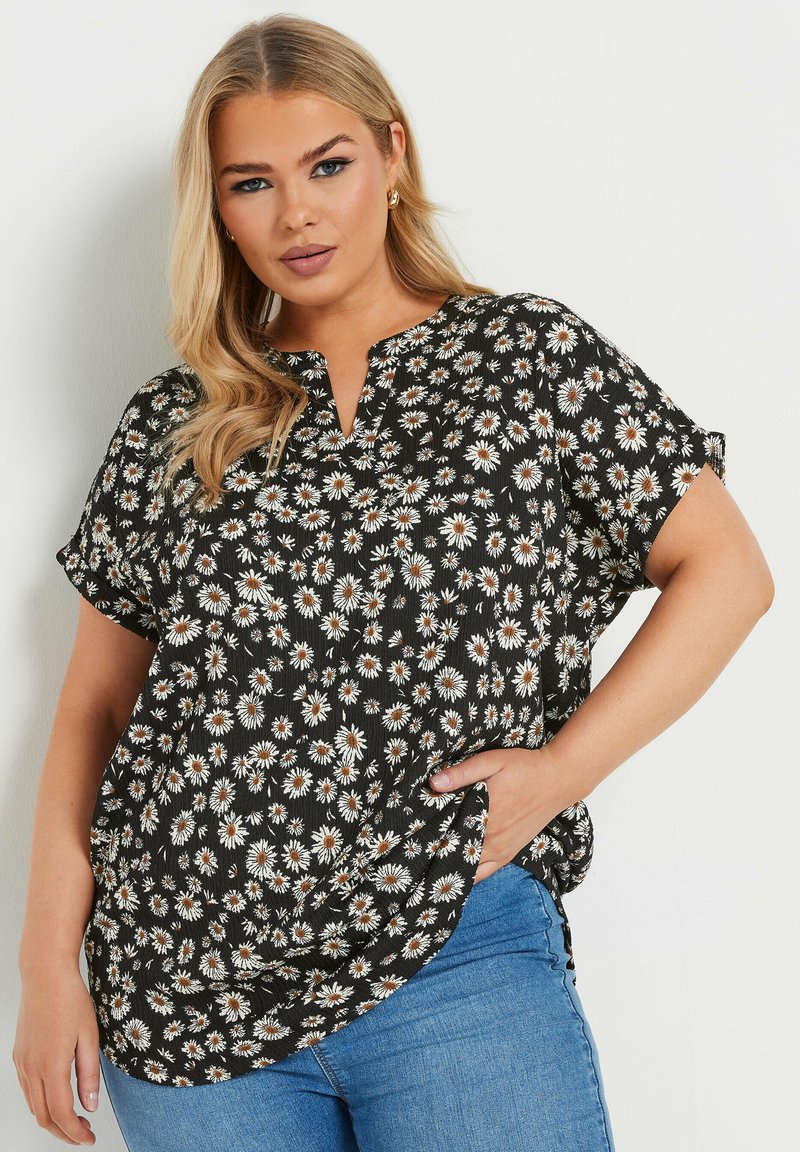 Blusa negra con estampado floral que presenta mangas cortas, un cuello en pico y patrones de margaritas blancas. Fabricada en una tela ligera con un corte holgado.