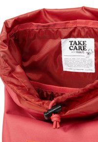 Bolsa de tela roja con cordón, de textura suave, que presenta una etiqueta blanca con texto negro. El forro interior también es rojo, lo que ofrece un aspecto cohesivo.