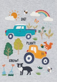 Gestickter Patch mit einem türkisfarbenen Lkw, einem orangenen Traktor, Bäumen, einem Hund und verschiedenen Naturelementen auf einem grauen Stoffhintergrund.