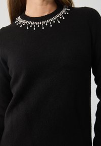 Schwarzer Pullover mit rundem Ausschnitt, verziert mit einem dekorativen Kragen aus Kristallperlen und aus einem weichen, strukturierten Stoff gefertigt.