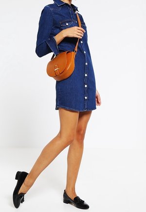 Woman wearing a buttoned blue denim dress with black loafers, carrying a brown leather crossbody bag over the shoulder.