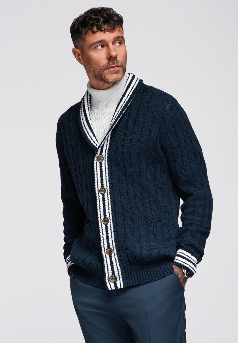 Cardigan a coste navale con colletto a scialle, dettagli a strisce bianche su polsini e patta, dotato di bottoni in legno e tasche laterali.