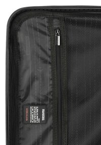 Interior de equipaje negro con un bolsillo de malla, forro interior gris con rayas diagonales y un compartimento con cremallera. Etiqueta visible.
