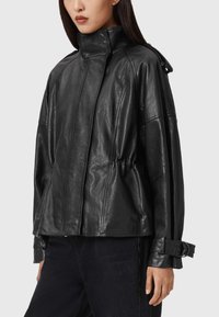 Zwarte leren jas met een hoge kraag, een relaxte pasvorm, een tailleband en overgrote mouwen. Voorzien van gespdetails op de manchetten.