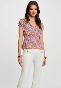 Haut peplum avec un motif zigzag coloré en rose, bleu et jaune ; manches courtes ; taille cintrée ; associé à un pantalon évasé blanc.