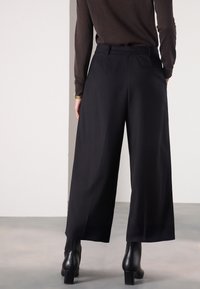 Sorte bukser med vide ben i glat stof, med høj talje, lommer og skræddersyet pasform, kombineret med sorte støvler med hæl.