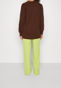 Hnědý pletený svetr s žebrovaným lemem, doplněný jasně limetkově zelenými kalhotami s volným střihem a dlouhými rukávy.