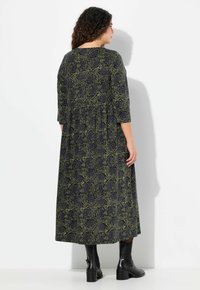 Dlouhá maxi šaty s dlouhým rukávem v černé barvě s zeleným růžovým vzorem, s nařaseným pasem a volným střihem. Nošeno s černými kotníkovými botami.