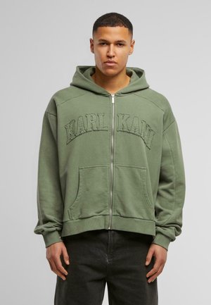 Green zip-up hoodie with a kangaroo pocket. Features embroidered "KARL KANI" on the front and a soft texture. Loose fit with a hood.