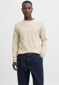 Beige Pullover mit langen Ärmeln und rundem Ausschnitt, weicher Textur. Trägt dazu eine dunkelblaue Hose und einen braunen Ledergürtel mit einer silbernen Schnalle.