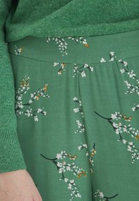 Grön tröja i kombination med en grön, blommönstrad klädesplagg med vita och orange blommor, slät textur och en figurnära midja.