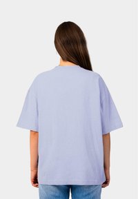 Lichtpaars oversized T-shirt, korte mouwen, geribbelde textuur, ronde halslijn, weergegeven vanaf de achterkant met blauwe spijkerbroek.