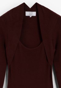 Suéter de punto burdeos con escote ancho y abertura frontal. Presenta textura acanalada y una etiqueta en la parte trasera.