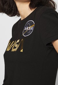 Camiseta de algodón negra con un logo dorado de "NASA" y un parche bordado circular de NASA con un diseño en blanco y dorado.