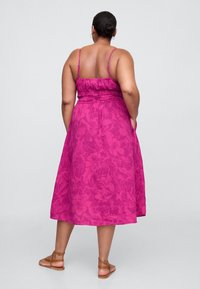 Fuksijos spalvos su gėlių raštais suknelė su reguliuojamomis plonomis petnešėlėmis, suveržta juosmeniu ir laisvai krintančia, iki kelių siekiančia sijono dalimi. Ruda lygios basutės pabrėžia išvaizdą.