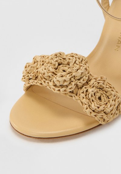 Woven straw sandal featuring two flower-shaped accents in natural beige. Smooth leather footbed with a flat sole. Simple, open design.