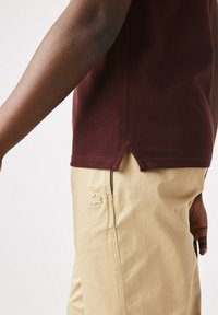 Burgundyrandig polo-skorta med sidofickor stoppad i beige byxor med en diskret logotypbroderi på låret för extra detalj.