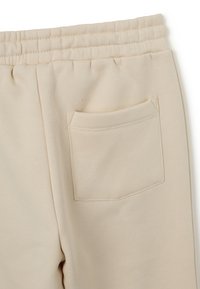 Beige Sporthosen mit einer weichen Textur, elastischem Bund und einer einzelnen Gesäßtasche mit sichtbaren Nahtdetails.