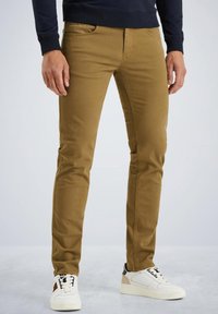 Pantalons slim fit kaki avec une texture lisse, des poches avant et des détails de couture subtils, associés à des baskets blanches avec des accents noirs et beiges.