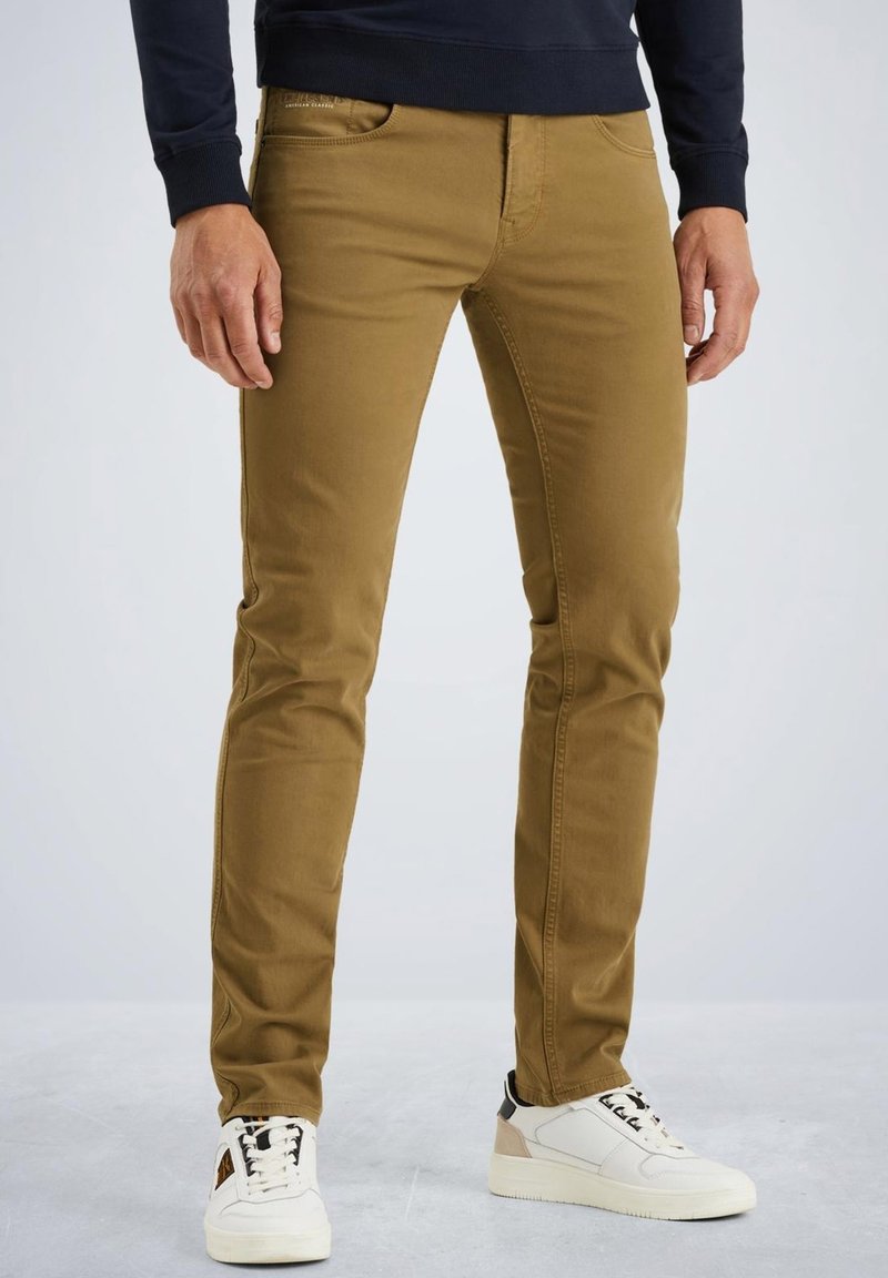 Pantalons slim fit kaki avec une texture lisse, des poches avant et des détails de couture subtils, associés à des baskets blanches avec des accents noirs et beiges.