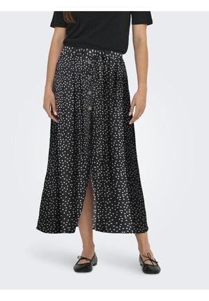 Mujer con falda midi negra con lunares blancos, botones delanteros, cintura elástica, combinada con bailarinas negras y una camiseta negra.