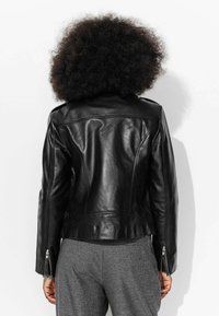 Veste en cuir noir avec coupe cintrée, poignets zippés et design épuré. Surface lisse avec un minimum de coutures et sans matériel visible.