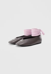 Pair of dark brown ballet flats with pointed toes and wide pink ankle ribbons wrapped around the top edges, against a white background.